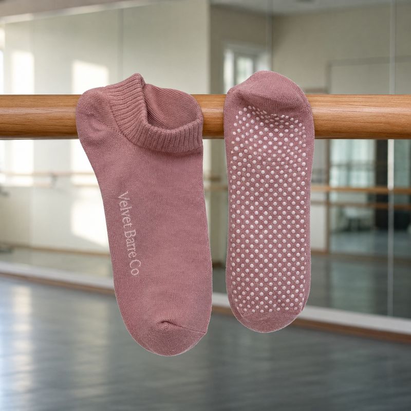 Custom grip socks for barre studios draped over a wooden ballet barre